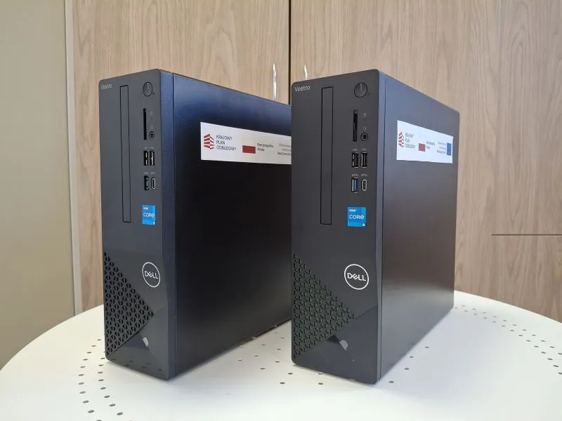 Dwa czarne komputery stacjonarne Dell Vostro ustawione pionowo na białym stole.