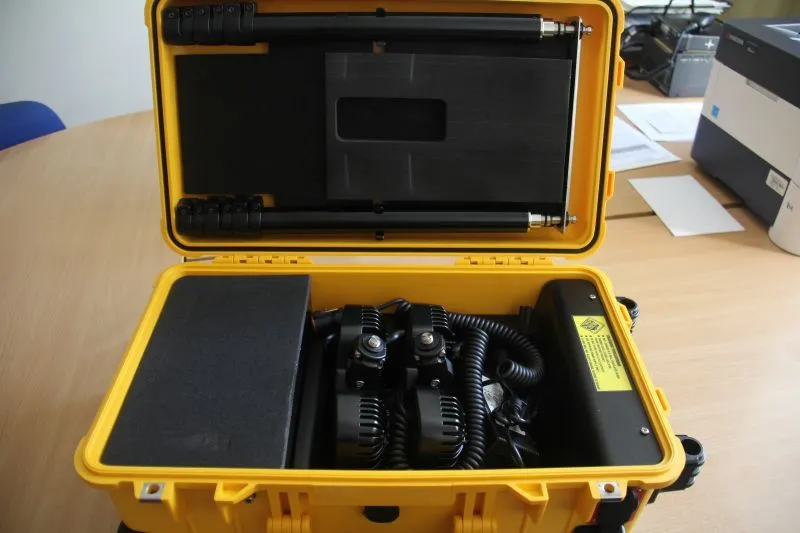 Żółta, zamknięta walizka zawierająca dwa czarne urządzenia z przewodami oraz akcesoria, ustawiona na drewnianym stole.