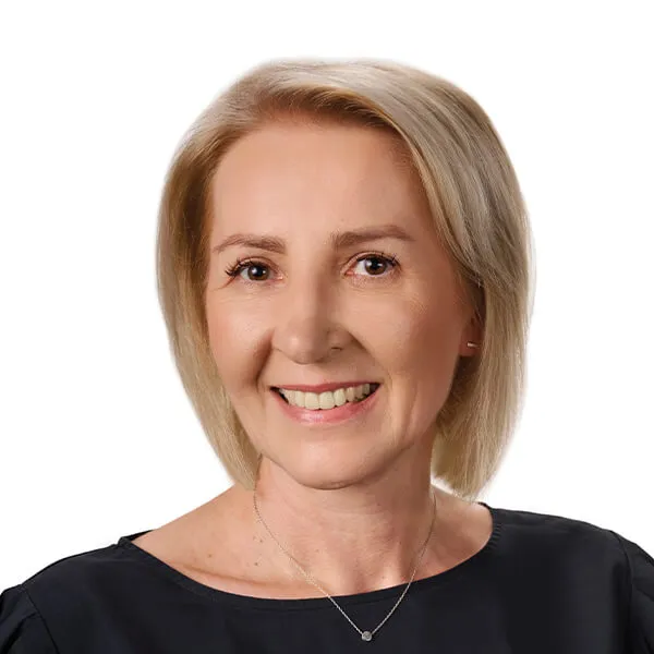 Kobieta z krótkimi blond włosami, uśmiechnięta, ubrana w czarną bluzkę i nosząca delikatny naszyjnik.