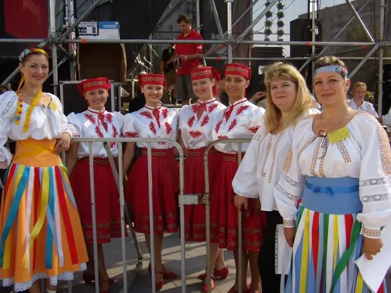 Grupa kobiet w tradycyjnych strojach ludowych stoi za barierką na tle sceny.