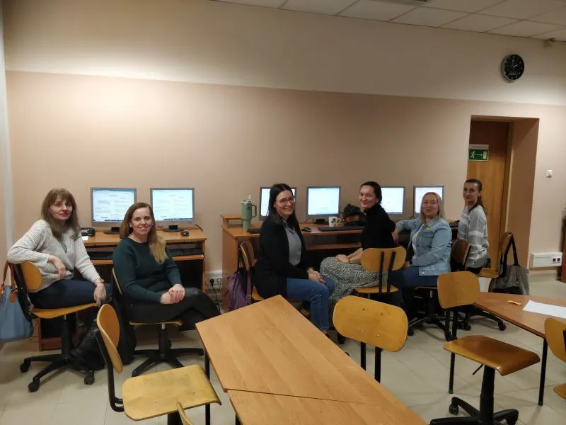 Sześć kobiet siedzi na krzesłach przy biurkach z komputerami w pomieszczeniu biurowym.