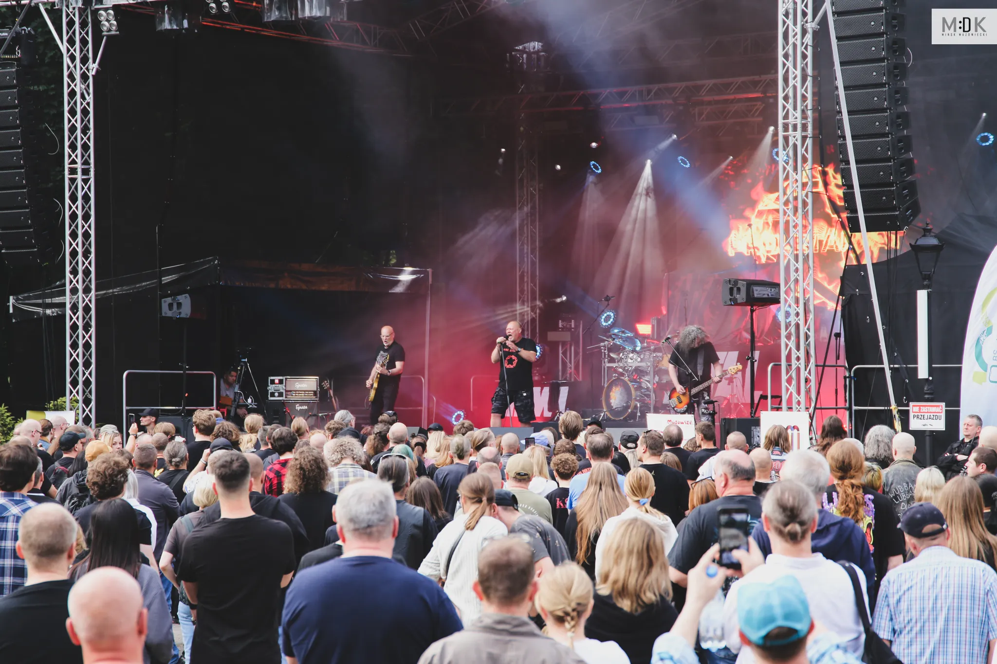 Publiczność ogląda koncert rockowego zespołu na oświetlonej scenie z gitarzystami i perkusistą.