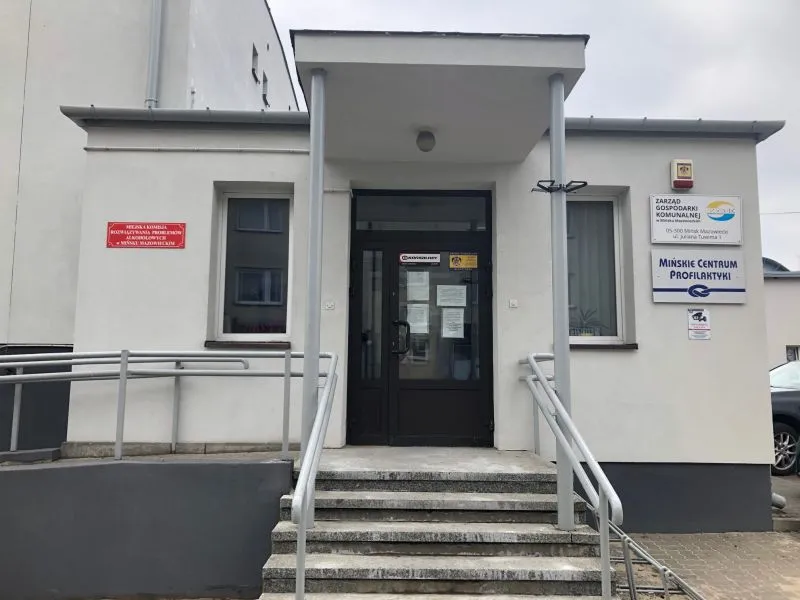 Wejście do budynku z podjazdem i schodami oraz tablicami informacyjnymi przy drzwiach.