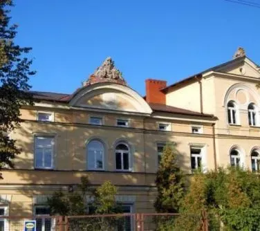 Dwupiętrowy żółty budynek z oknami o zaokrąglonych łukach i ozdobnym przyczółkiem na dachu.