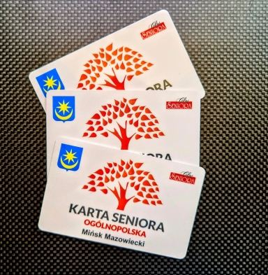 Trzy białe karty „Karta Seniora Ogólnopolska” z czerwonym logo drzewa i symbolem herbu Mińska Mazowieckiego na czarnym tle.