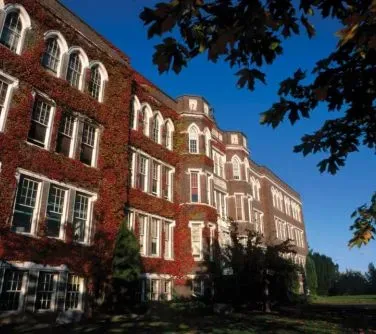 Czteropiętrowy budynek z czerwonej cegły z licznymi oknami i częściowo porośnięty pnączami.