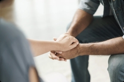 Dłonie dwóch osób trzymające się wzajemnie na tle jasnej powierzchni.