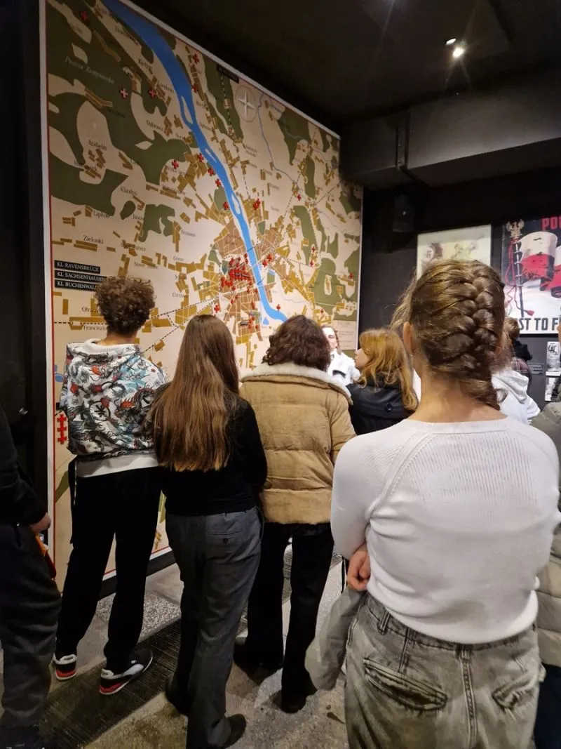 Grupa ludzi stoi przed dużą mapą zawierającą oznaczenia miast i rzek.