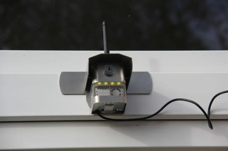 Zamontowana na białej powierzchni kamera monitoringu z anteną i podłączonym kablem.