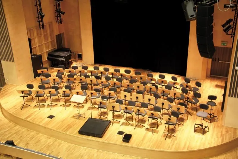 Scena z ustawionymi krzesłami i pulpitami dla muzyków, statywem na nuty oraz głośnikami.