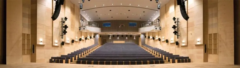 Sala teatralna z rzędem niebieskich foteli, balkonem i systemem nagłośnienia.