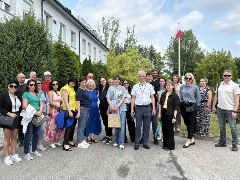 Grupa dorosłych osób stojących razem na chodniku przed budynkiem i drzewami.