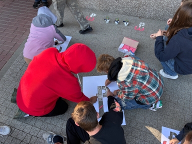 Grupa dzieci malujących litery na szablonach na chodniku podczas dnia.