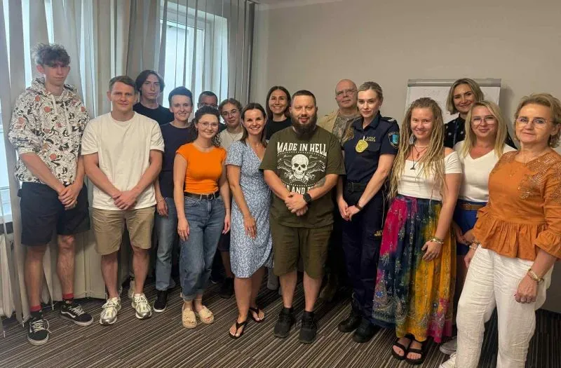 Grupa osób w różnym wieku pozuje do zdjęcia w pomieszczeniu z wykładziną.