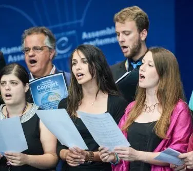 Grupa osób trzymających śpiewniki i śpiewających razem.