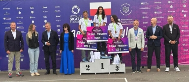 Trzy kobiety z medalami stoją na podium z nagrodami pieniężnymi za Roller Freestyle, wokół nich stoi osiem osób na tle fioletowej ścianki z logo World Skate Europe i polskiej flagi.