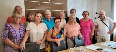 Grupa jedenastu osób stoi w sali konferencyjnej przy stole z kawą, notatnikami i dokumentami.