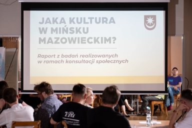 Grupa osób siedzi w sali konferencyjnej, na ekranie wyświetla się tytuł prezentacji dotyczącej kultury w Mińsku Mazowieckim w ramach konsultacji społecznych.