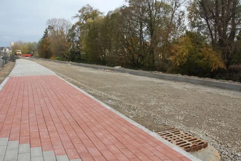 Nowa kostka brukowa po lewej stronie i nierówna nawierzchnia drogi po prawej stronie z kratką odpływową na pierwszym planie.