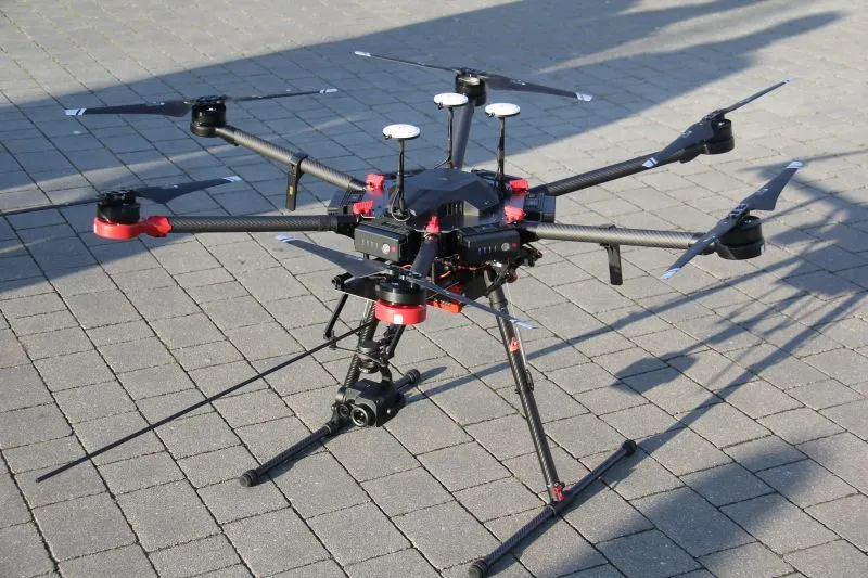 Sześciośmigłowy dron z kamerą zamocowaną pod spodem stoi na kostce brukowej.