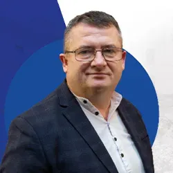 Mężczyzna w okularach ubrany w biały garnitur i marynarkę w kratę na tle w odcieniach niebieskiego.