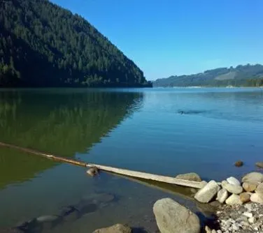 Spokojna tafla jeziora z uchwyconym kawałkiem drewnianej kładki i kamieniami na brzegu.