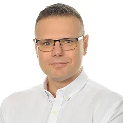 Mężczyzna w białej koszuli i okularach, z krótkimi, zaczesanymi włosami, na białym tle.