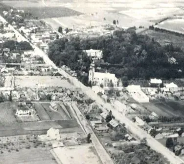 Widok z lotu ptaka na wiejskie zabudowania z drogą przebiegającą przez centrum oraz kościołem otoczonym drzewami.