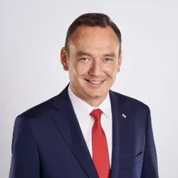 Mężczyzna w garniturze z czerwonym krawatem i przypinką w kształcie flagi Polski.